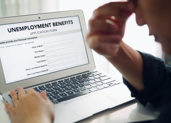 Unemployed depressed person filling out an online unemployment benefits application form using laptop computer.