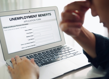 Unemployed depressed person filling out an online unemployment benefits application form using laptop computer.