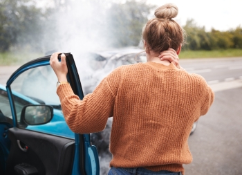 Rear View Of Female Motorist With Head Injury Getting Out Of Car After Crash