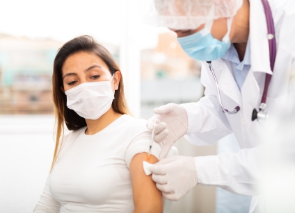 doctor in protective face mask vaccinates woman